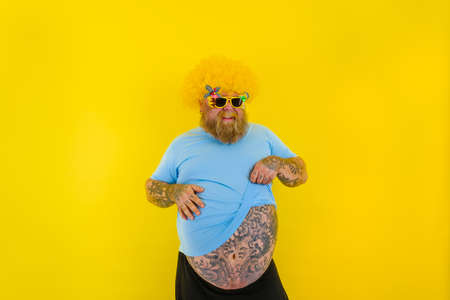 Fat man with wig in head and sunglasses shows off her big bellyの写真素材