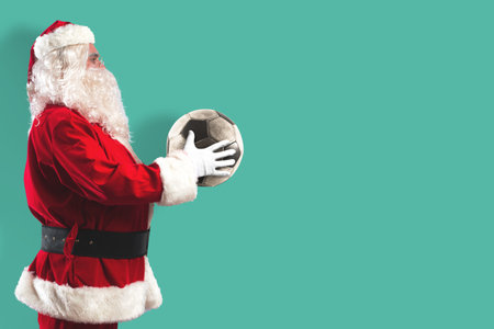 Santa Claus with a soccer ball in his hands isolated on a mint colored backgroundの写真素材