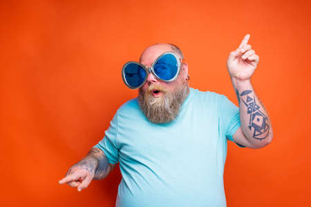 Fat amazed man with beard, tattoos and sunglasses dances musicの写真素材