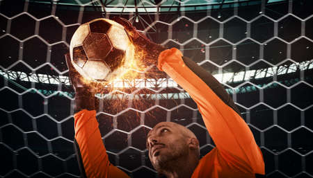 Close up of a soccer scene at night match with a goalkeeper trying to catch a fiery ball