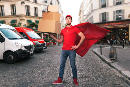 Superhero man with red uniform in front of the shops for delivery and pickup of the goodsの写真素材