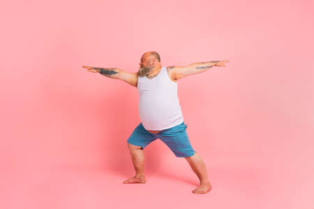 Funny man with beard in yoga position on studio pink backgroundの写真素材