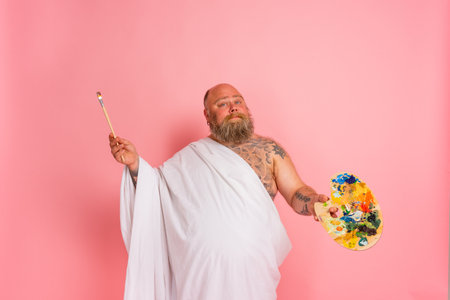 Fat man acts like an important artist with brush and color set in handの写真素材