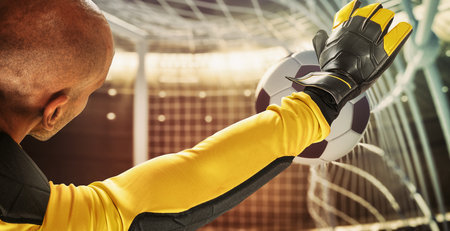 Goalkeeper catches the ball in the stadium during a football gameの写真素材