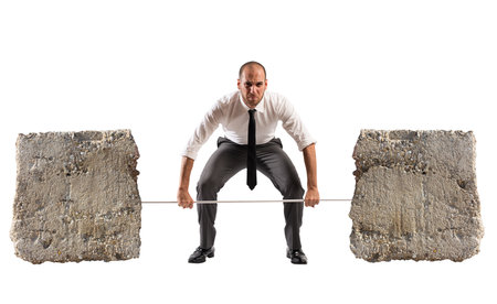 Powerful and determined businessman trains with a barbell with stonesの写真素材