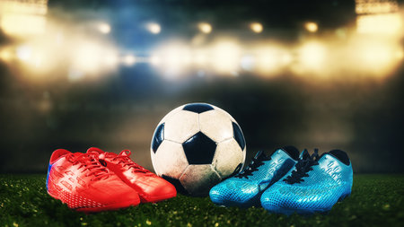 Two pairs of soccer shoes and a ball on the ground as a sign of challengeの写真素材