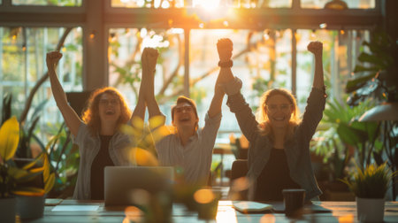 Business team celebrating a victory with raised arms in a modern workplace at sunsetの素材