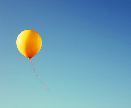 Bright yellow balloon floats against a clear blue sky on a sunny dayの素材
