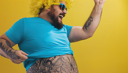 Man with yellow wig dances with joy in front of yellow wall during a fun celebrationの素材