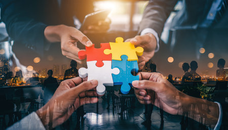 Hands join colorful puzzle pieces during a business meeting at night in a city skylineの素材