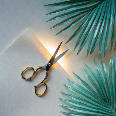 Creative scene with scissors placed near green palm leaves on a white surface in a bright light settingの素材