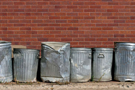 line of metal trash cans against a red brick wallの写真素材
