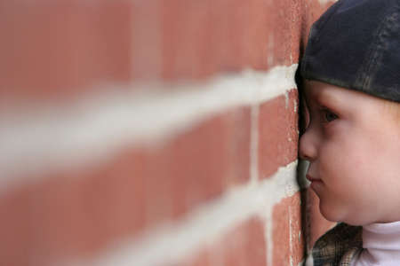 cute redheaded kid wearing a baseball cap, stands with his nose squished against a red brick wall. heaps of copyspace.の写真素材
