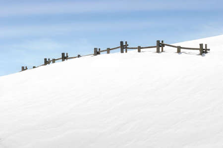 fence on snowy hill with blue skyの写真素材