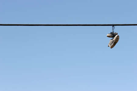 shoes on power lines - urban scene, worn tennis shoes hanging from a power line against clear blue sky. plenty of copyspace.の写真素材