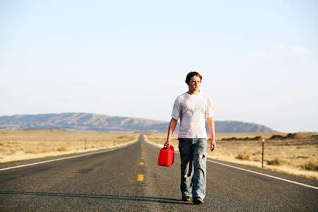 out of gas - teenager male walking down rural highway with empty red gas canの写真素材