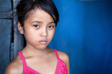 Young Filipina girl 8 years old with sad and somber expression over blue, poverty in the Philippines.の写真素材