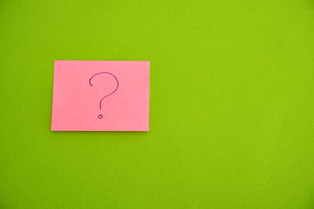 Question mark on pink sticky note isolated on green background with copy spaceの写真素材