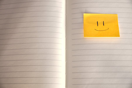 Yellow sticky note with smiley face on notebook page, closeupの写真素材