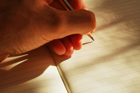 Hand writing on a notebook with light and shadow in the background.の写真素材