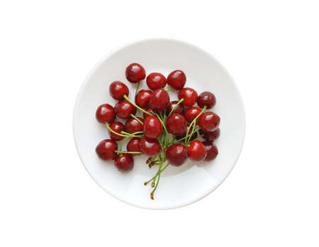 Wet red cherries on a white round plate isolated on a white background. Top view