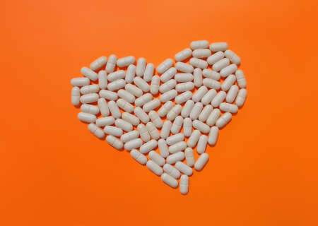 Heart of white pills on vivid orange background. The concept of dietary supplements.の写真素材