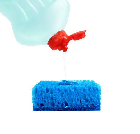 Dishwashing liquid is poured from a blue plastic bottle with a red cork on a blue rectangular sponge. Isolated on a white backgroundの写真素材