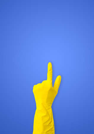 Hand in yellow rubber gloves points up on a blue background with a copy spaceの写真素材