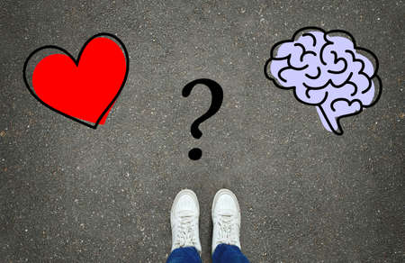 Heart or brain? Legs in white sneakers in front of heart and brain symbols with a question mark between them on the gray asphalt background. Path choice conceptの写真素材