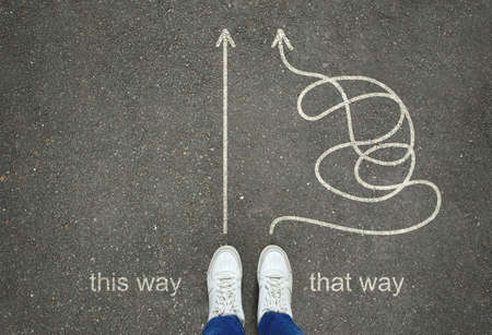 Legs in white sneakers in front of straight and tangled arrows leading to the same goal on the gray...