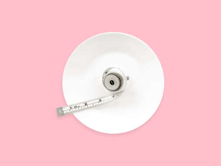 White measuring tape in a white round plate on a pink background. Top viewの写真素材