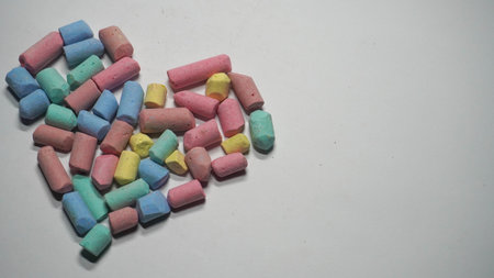 A collection of vibrant chalk pieces organized into a heart shape, symbolizing creativity and art. The colorful arrangement on a clean white surface evokes feelings of fun, creativity, and loveの写真素材