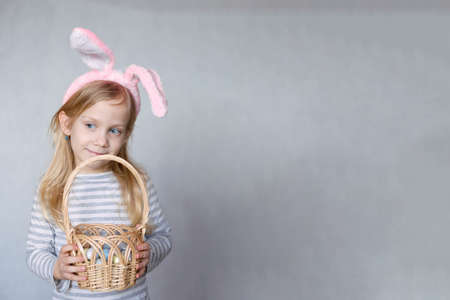 blonde girl in a striped jacket, on a bright background, with rabbit ears on her head, holding a...