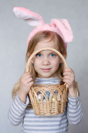 blonde girl in a striped jacket, on a bright background, with rabbit ears on her head, holding a...