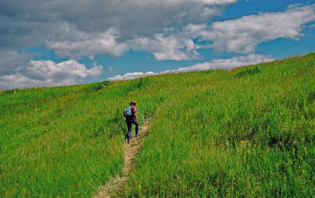 A girl tourist climbing a hillside with a backpack.の写真素材