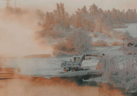 Old excavator among frozen trees. Mysterious fog above the river in industrial landscape