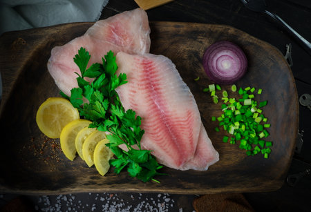 Fresh tilapia fish fillet with ingredients for cooking on the cutting board. Top view.の写真素材