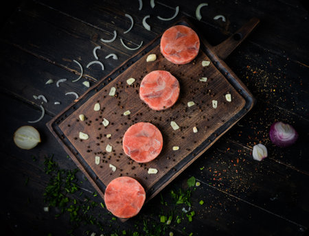 Raw fresh salmon medallions with garlic and onion on wooden cutting board. Top viewの写真素材