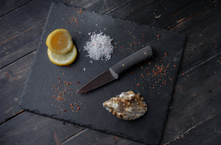 Oyster knife on on a black stone background with lemon and spices. Top viewの写真素材