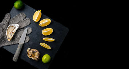 Fresh oysters on a black stone background. Oyster dinner in restaurant. Dark background. Seafood, Gourmet food. Oyster glove, oyster opening knife. Top View with Copy space.の写真素材