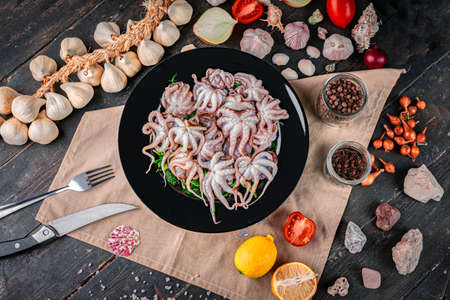Raw baby octopus in a black plate. Organic seafood. Top view.