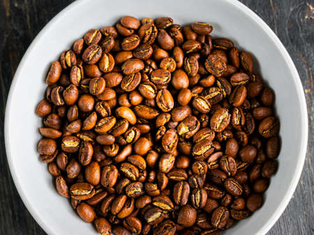 Coffee beans in a bowl on a wooden background. Roasted black coffee in a dish.
