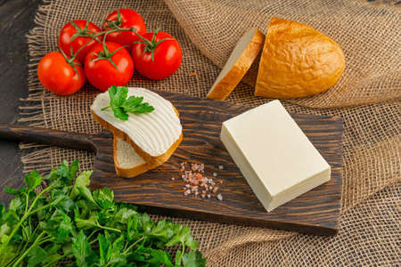 Tasty bread with butter on wooden cutting board. A large piece of butter.の写真素材