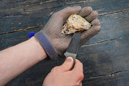Opening fresh oyster with knife. Hand in protective gloves.の写真素材
