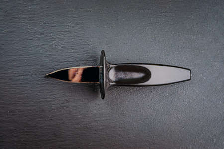 A black oyster knife on a slate slab.