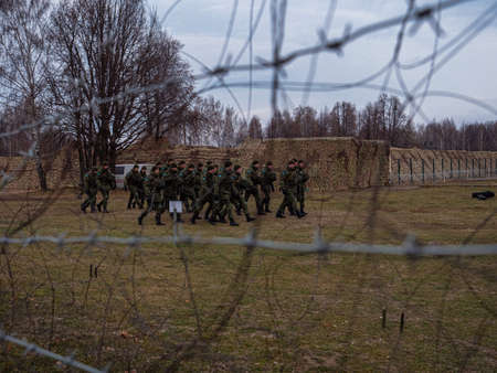 Soldiers of the Russian army walking across a field. View through barbed wire.のeditorial素材