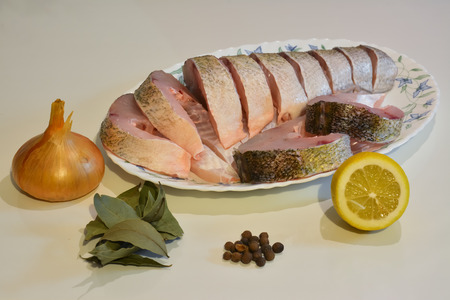 Sliced fish on a plate for cooking, onion, pepper, laurel leaf, lemon.の写真素材