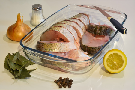 Sliced fish in a glass tray, knife, salt and spices around.の写真素材