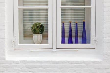 Design of the window. White wall, window, blue bottle, flower in ceramic potの写真素材