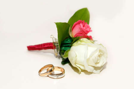 beautiful groom's boutonniere of white and red roses and wedding rings on a white table
